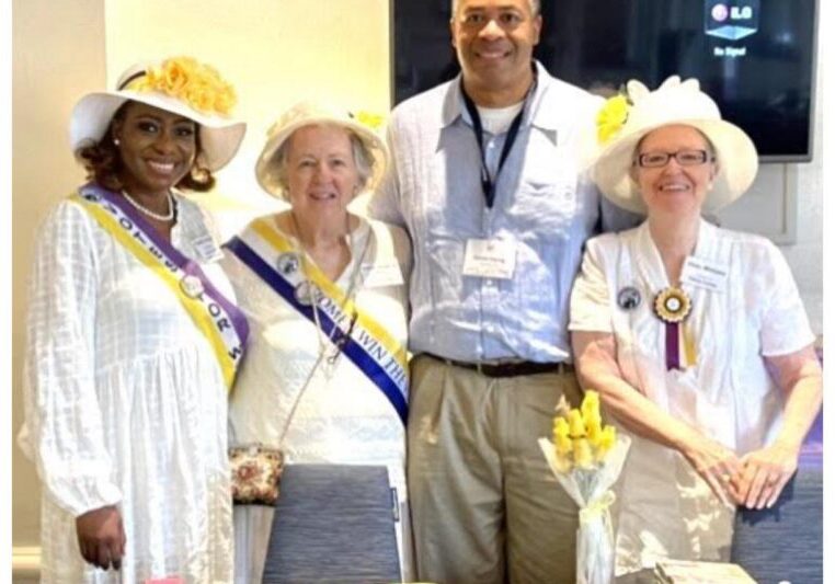 Four smiling people wearing hats and sashes at an event.