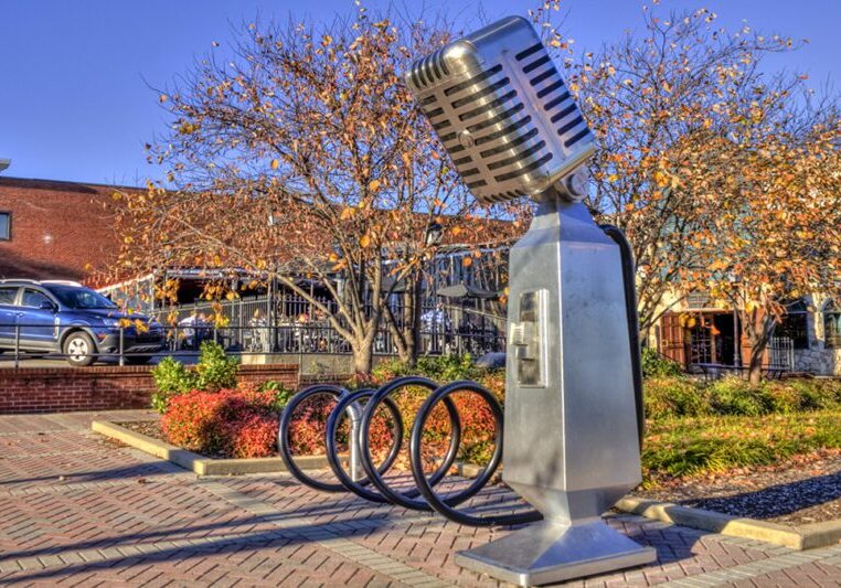 A giant retro microphone sculpture outdoors with bike racks and autumn trees.