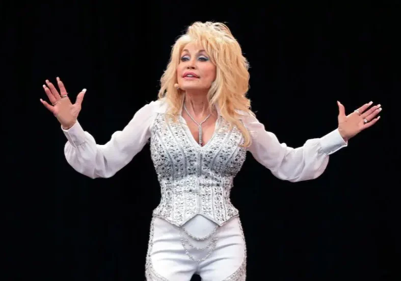 Dolly Parton performing on stage in a sparkling white outfit.