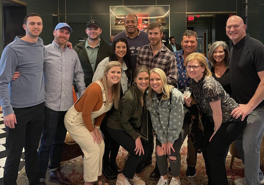 A large group poses together indoors on a checkered floor.