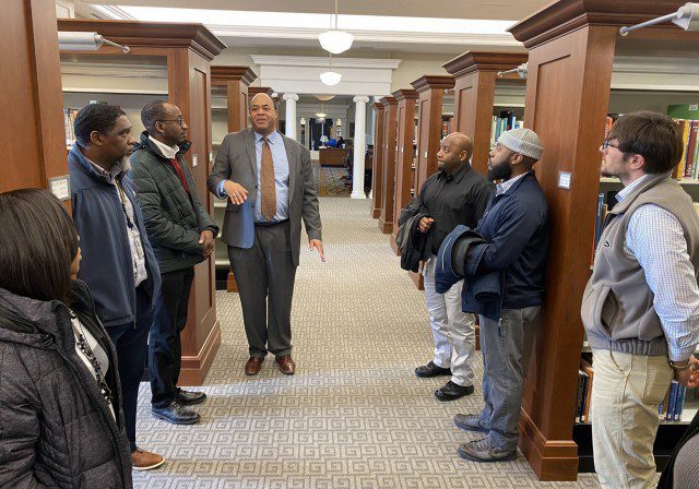 People standing and conversing in a hallway lined with wooden cabinets.