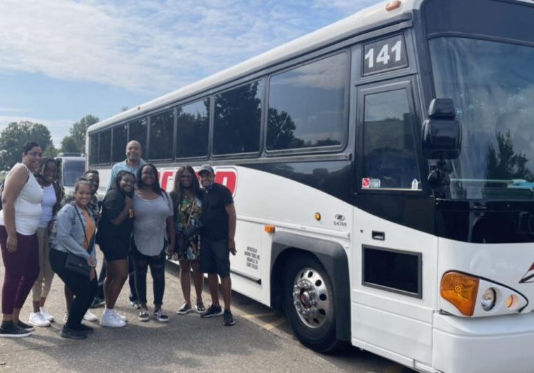 A group of people posing beside a large black and white bus on a sunny day.