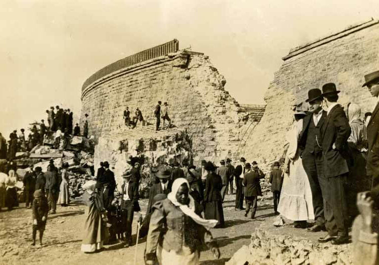 Historical photo of people near ancient ruins, depicting daily life.