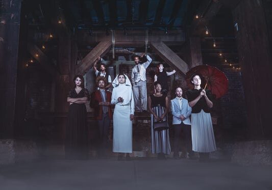 A group of people in vintage clothing posing dramatically in a dimly lit attic.