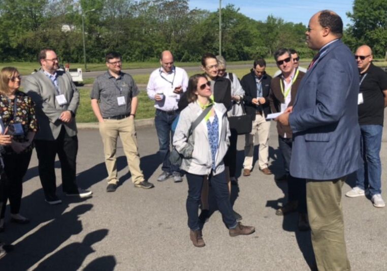 A group of people outdoors, with one person speaking into a microphone.